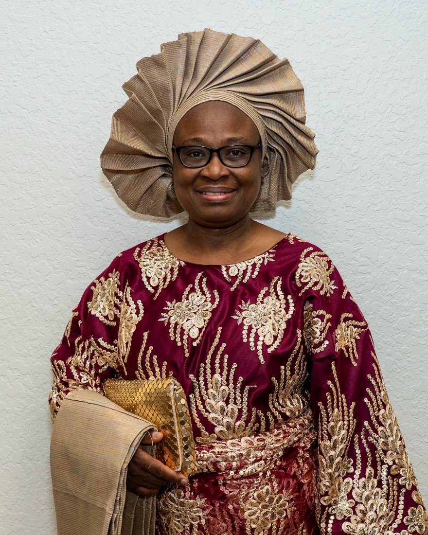 Clementine Amondi, smiling, in a burgundy and gold lace dress and a gold head-wrap